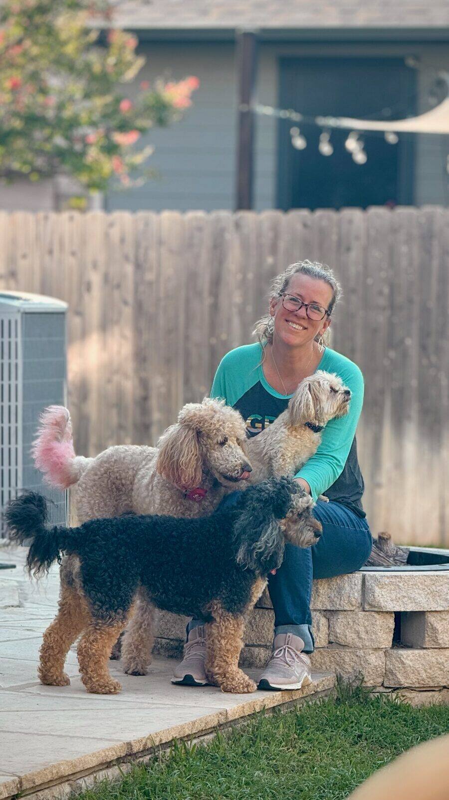 Heather smiling in the backyard with two well-groomed poodles